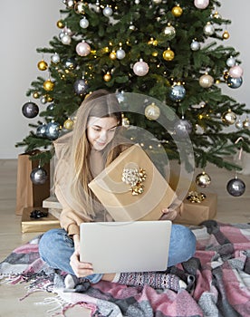 Teenage girl with gifts and laptop near the Christmas tree