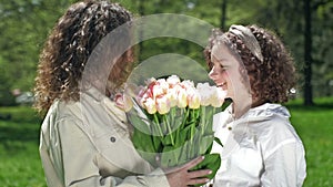 Teenage girl gives her mother a large beautiful bouquet of tulips. Mother hugs daughter. Mothers Day.
