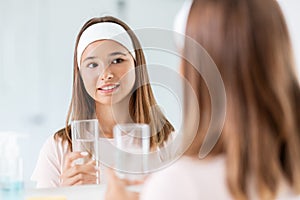 teenage girl with glass of water looking in mirror