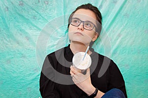 A teenage girl with glasses holds a paper Cup of soda in her hand and looks thoughtfully at the top