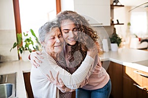 A teenage girl with grandmother at home, hugging.