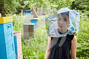 Teenage girl in hat with bee veil stands at apiary photo