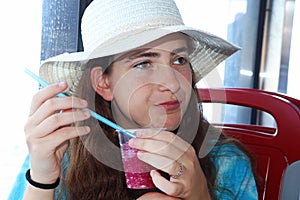 A teenage girl with a hat drinks a red cold drink