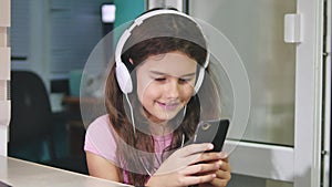 Teenage girl with headphones sitting with plays a smartphone. schoolgirl girl playing online game on indoors smartphone