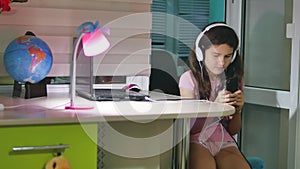 Teenage girl with headphones sitting with plays a smartphone. schoolgirl girl playing online game on indoors smartphone