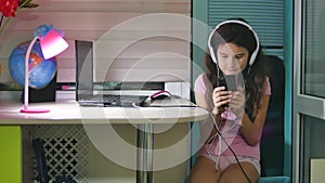 Teenage girl with headphones sitting with plays a smartphone. schoolgirl girl playing online game on smartphone indoors