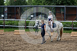 A teenage girl in a helmet is learning to ride a horse. An instructor teaches teenagers how to ride a horse.