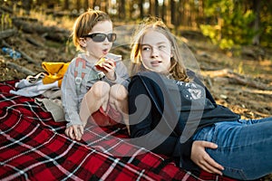 Teenage girl on her little brother having a picnic on the lake shore under pine trees. Siblings having good time bonding outdoors