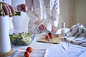 a teenage girl and her mother in pajamas are cooking and eating a fresh green and tomato salad together