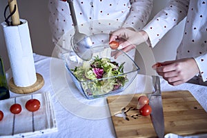 a teenage girl and her mother in pajamas are cooking and eating a fresh green and tomato salad together