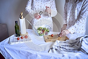 a teenage girl and her mother in pajamas are cooking and eating a fresh green and tomato salad together