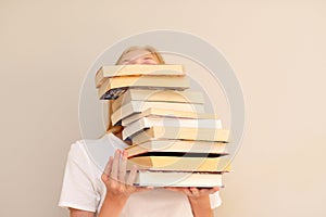 Teenage girl hiding behind big pile of books she wants to read