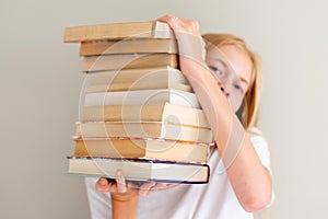 Teenage girl hiding behind big pile of books she wants to read. Student ready to study concept