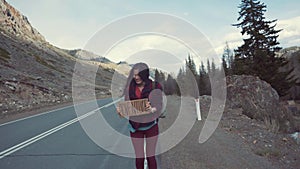 Teenage Girl Holding An Adventure Sign On A Mountain Road, Smiles And Laughs. Hitchhiking in search of adventure.