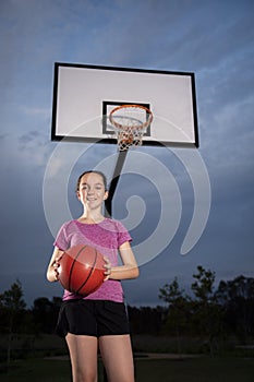 Teenage girl holding a basketball at an outdoor court