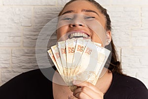 Teenage girl holding brazilian banknotes currency. Financial, profit, credit, cost, purchase, rich