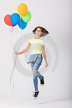 Teenage girl holding a bunch of balloons jumps in an empty room, copy space on the empty wall