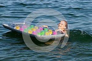 Teenage girl holding an inflatable mattress in the water and laughing