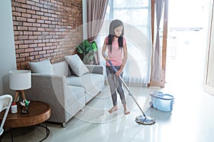 Teenage girl holding a mop stick doing household chores is mopping the living room