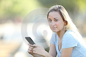 Teenage girl holding phone looking at camera in a park
