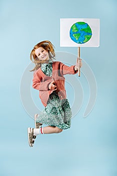 Teenage girl holding planet earth sign jumping in support of zero waste movement