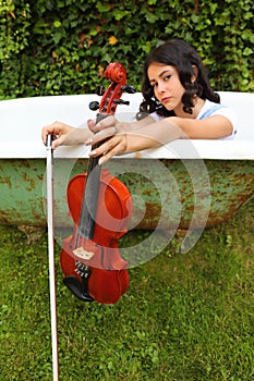 Teenage girl holding violin and fiddlestick outdoor in bathtub