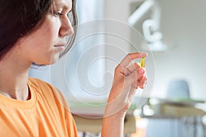 Teenage girl holding yellow vitamin d gel capsule in hand, dentist office background