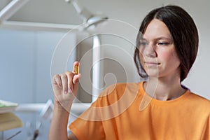 Teenage girl holding yellow vitamin d gel capsule in hand, dentist office background