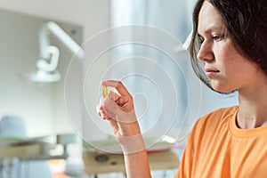 Teenage girl holding yellow vitamin d gel capsule in hand, dentist office background