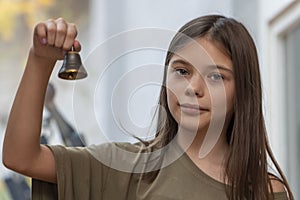 A teenage girl holds a bell in her hand on a blurry neutral background