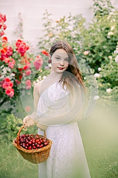 Teenage girl holds a cherry near her ears as if it were earrings, in her hands she has a basket of wild cherries