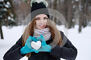 A teenage girl holds a heart made of snow in his hand