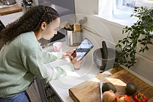 Teenage Girl At Home In Kitchen With Ingredients Looking At Recipe On Digital Tablet