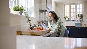 Teenage Girl At Home In Kitchen With Ingredients Looking At Recipe On Digital Tablet