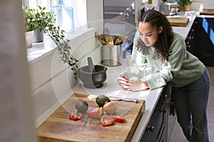 Teenage Girl At Home In Kitchen With Ingredients Looking At Recipe On Mobile Phone