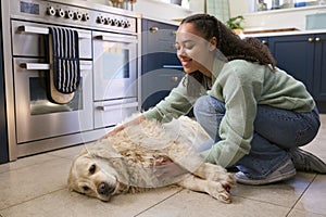Teenage Girl At Home In Kitchen Stroking Pet Golden Retriever Dog Lying On Floor