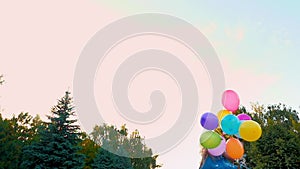 A teenage girl in jeans runs through the park with a large bunch of colorful balloons.