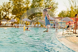 Teenage girl jumps into the water from the side of the pool