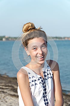 A teenage girl laughs contagiously against the backdrop of the sea coast.