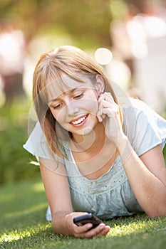 Teenage Girl Laying In Park Using Mobile Phone