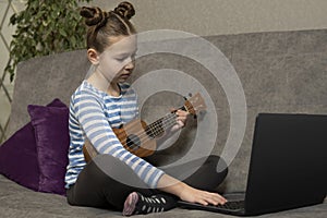 Teenage girl learns to play the ukulele and looks into her laptop.