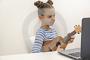 Teenage girl learns to play the ukulele and looks into her laptop.