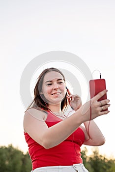 Teenage girl listening to the music in headphones in the park at sunset