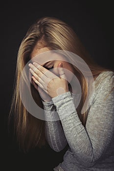 Teenage girl with long blond hair crying with her hands up to her face.