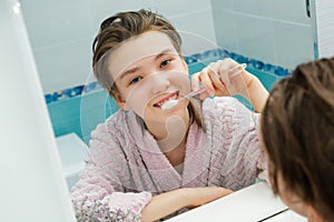 Teenage girl looks in the mirror, smiles and brushes teeth