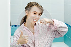 Teenage girl looks in the mirror, smiles and brushes teeth