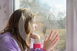 Teenage girl looks out window in morning. You can`t walk, sad emotions. Close-up, side view