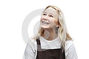 A teenage girl looks up and laughs. Cute blonde girl in a white T-shirt and brown overalls. White background