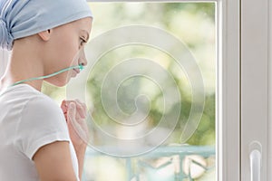 Teenage girl with lung cancer looking through the window in medical center