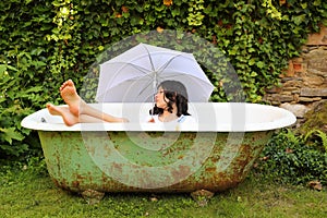 Teenage girl lying in bathtub with umbrella